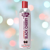 A bottle of Wet Warming Fun Flavors Black Cherry 4-In-1 Lubricant is set against a blurred background with colorful lights. The white bottle features red and black text along with cherry illustrations.